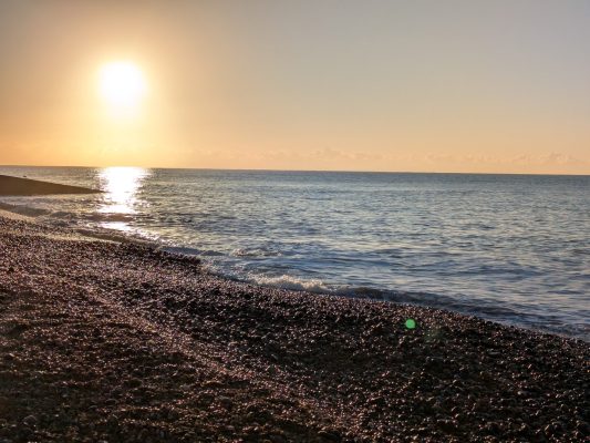 Golden sunrise over a pebbly beach, with a calm sea lapping at the shore