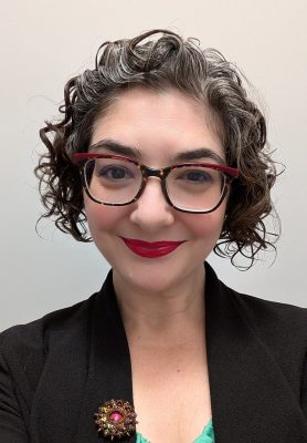 Photo of Tasha: a white woman with dark curly hair, big glasses, and red lipstick